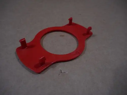Roter Rastring mit runder Öffnung und vier Haltefüßen, möglicherweise für einen Griff von Remeha-Geräten. Kunststoffoberfläche auf neutralem Hintergrund.